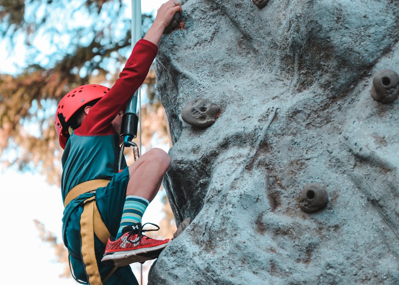 Young child rock climbing with safety gear, showcasing courage and determination.