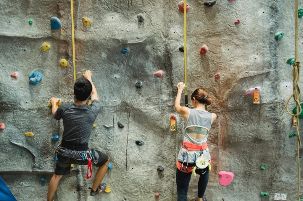 Back view of unrecognizable male and female alpinists in activewear and sit harness exercising on climbing wall in gym